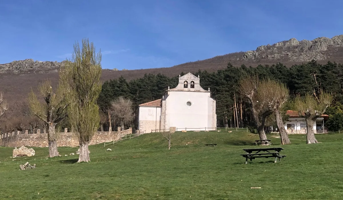 Ermita de Hontanares en Riaza, Segovia, rodeada de praderas verdes, árboles y montañas al fondo en un entorno natural y tranquilo