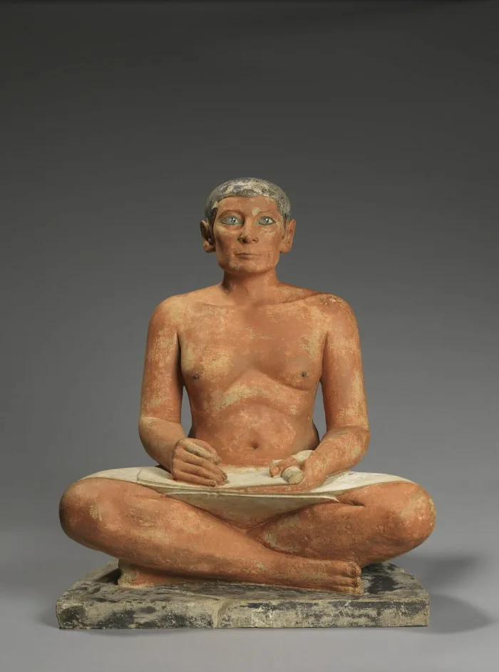 Escultura egipcia del Imperio Antiguo, datada alrededor del 2600-2350 a.C. Representa a un escriba en posición sedente con las piernas cruzadas y un rollo sobre las rodillas. Destaca por el realismo de su rostro y su mirada vívida, lo que la convierte en una de las piezas más célebres del arte egipcio conservadas en el Louvre.