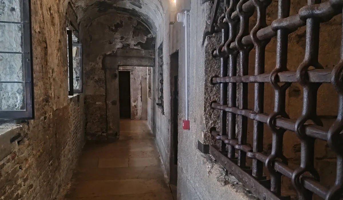 Pasillo abovedado del interior del Puente de los Suspiros en el Palacio Ducal de Venecia, iluminado tenuemente y flanqueado por rejas y puertas de madera.