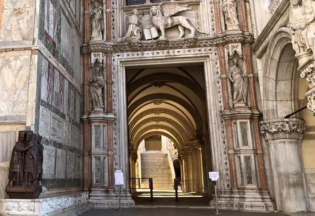 Puerta gótica del Palacio Ducal de Venecia con el relieve del dux arrodillado ante el León de San Marcos, rodeada de mármoles policromos y esculturas ornamentales.