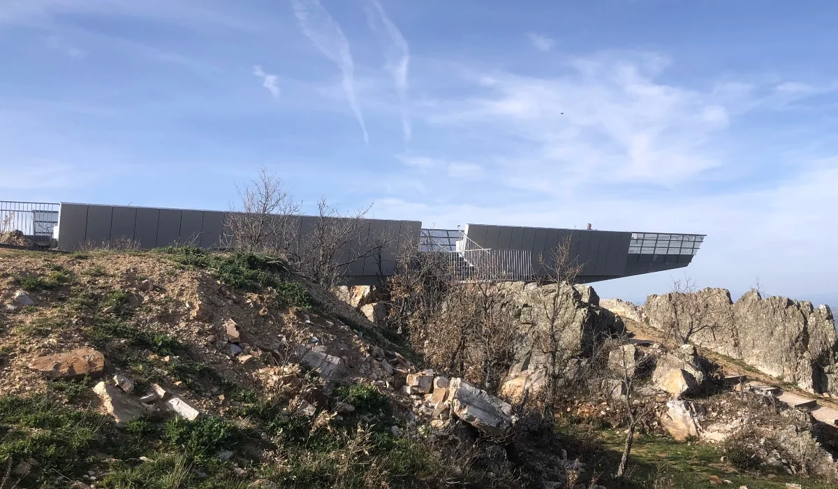Estructura metálica del Mirador de Peñas Llanas en Riaza (Segovia), sobresaliendo entre rocas y vegetación de montaña bajo un cielo azul despejado.