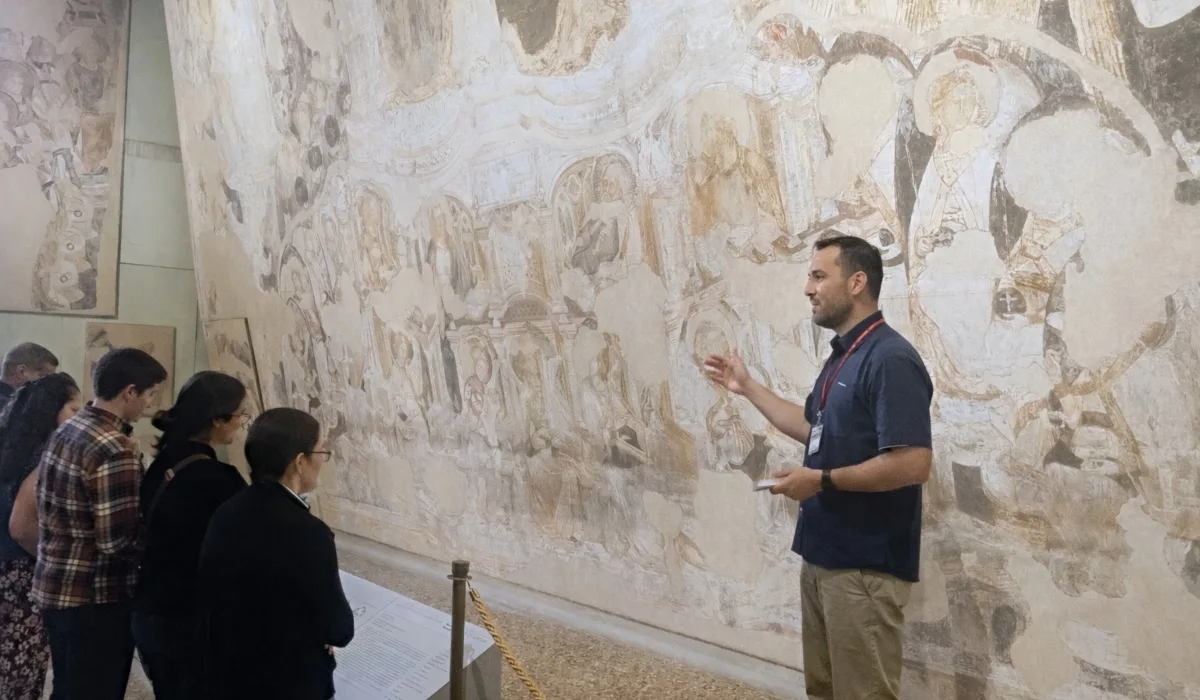 Guía turístico explicando frescos históricos en un museo de Venecia a un grupo de visitantes durante una visita cultural