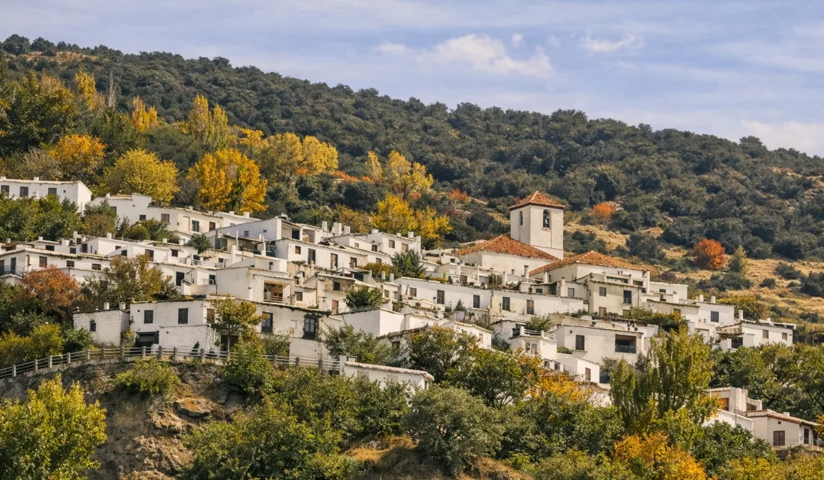 Casas blancas escalonadas de Capileira en la Alpujarra de Granada, con iglesia y campanario sobre la ladera y vegetación de montaña