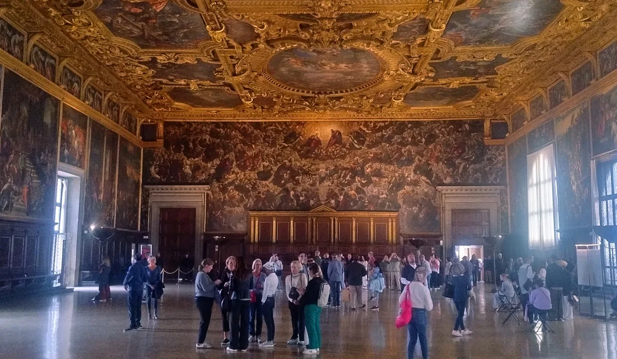 Visitantes recorriendo el Salón del Gran Consejo del Palacio Ducal de Venecia con techos dorados y frescos históricos
