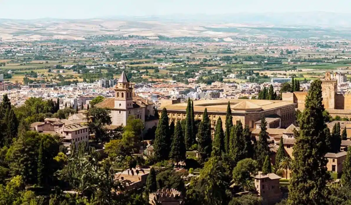 Vista panorámica de la Alhambra de Granada con la ciudad al fondo y la Vega de Granada extendiéndose hacia Sierra Nevada en un día despejado