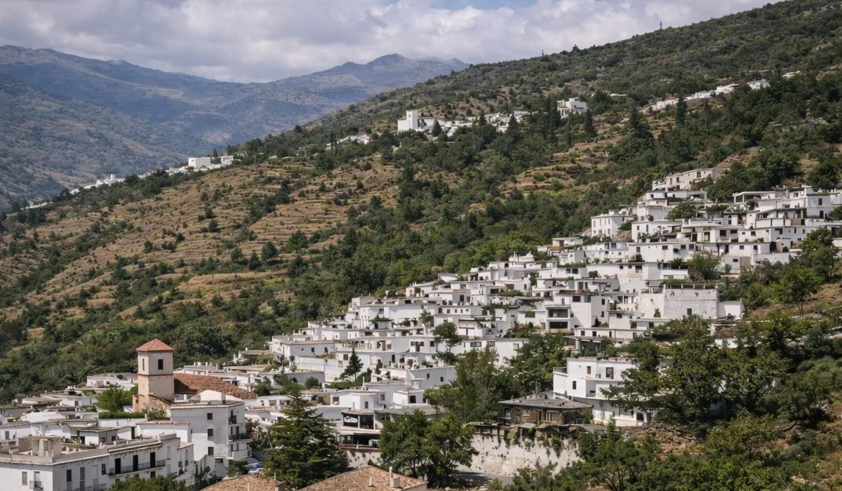 Vista panorámica de Pampaneira en la Alpujarra granadina, con casas blancas escalonadas, montañas de Sierra Nevada al fondo y cielo azul con nubes