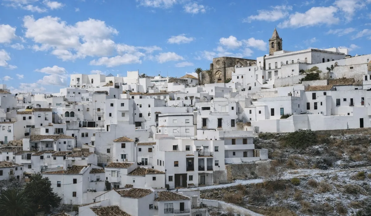 Vista panorámica de Vejer de la Frontera con casas blancas escalonadas, iglesia en lo alto del casco histórico y cielo azul con algunas nubes en la provincia de Cádiz.