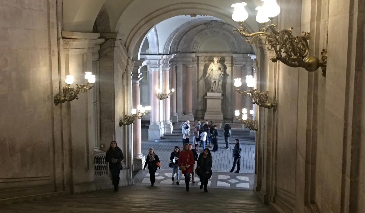 Escalinata interior del Palacio Real de Madrid con visitantes y estatua clásica al fondo