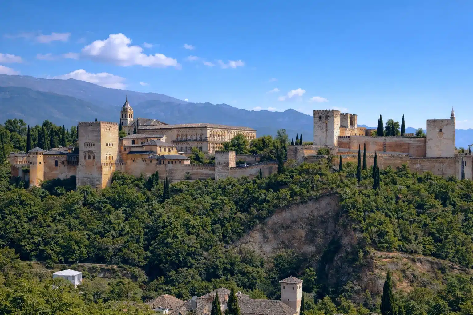 Vista panorámica de la Alhambra de Granada con la ciudad al fondo y la Vega de Granada extendiéndose hacia Sierra Nevada en un día despejado