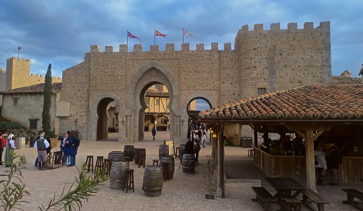 Puy du Fou España con murallas de piedra y visitantes en la plaza ambientada en época histórica.
