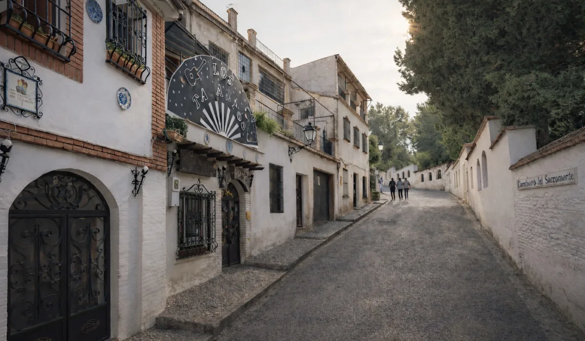 Camino del Sacromonte en Granada al atardecer, con casas blancas tradicionales, rejas de forja y luz cálida suave, calle en ligera pendiente y contraste bajo.
