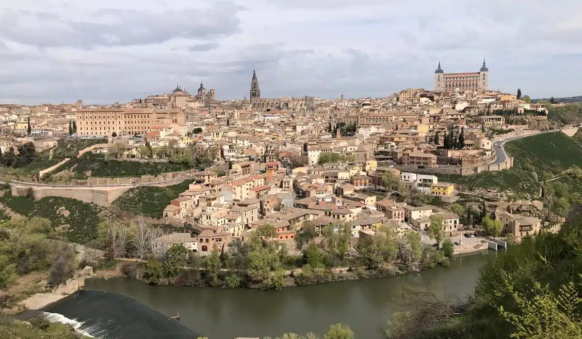 Panorámica histórica de Toledo con el río Tajo en primer plano, el casco antiguo amurallado, la Catedral de Toledo y el Alcázar dominando la ciudad.