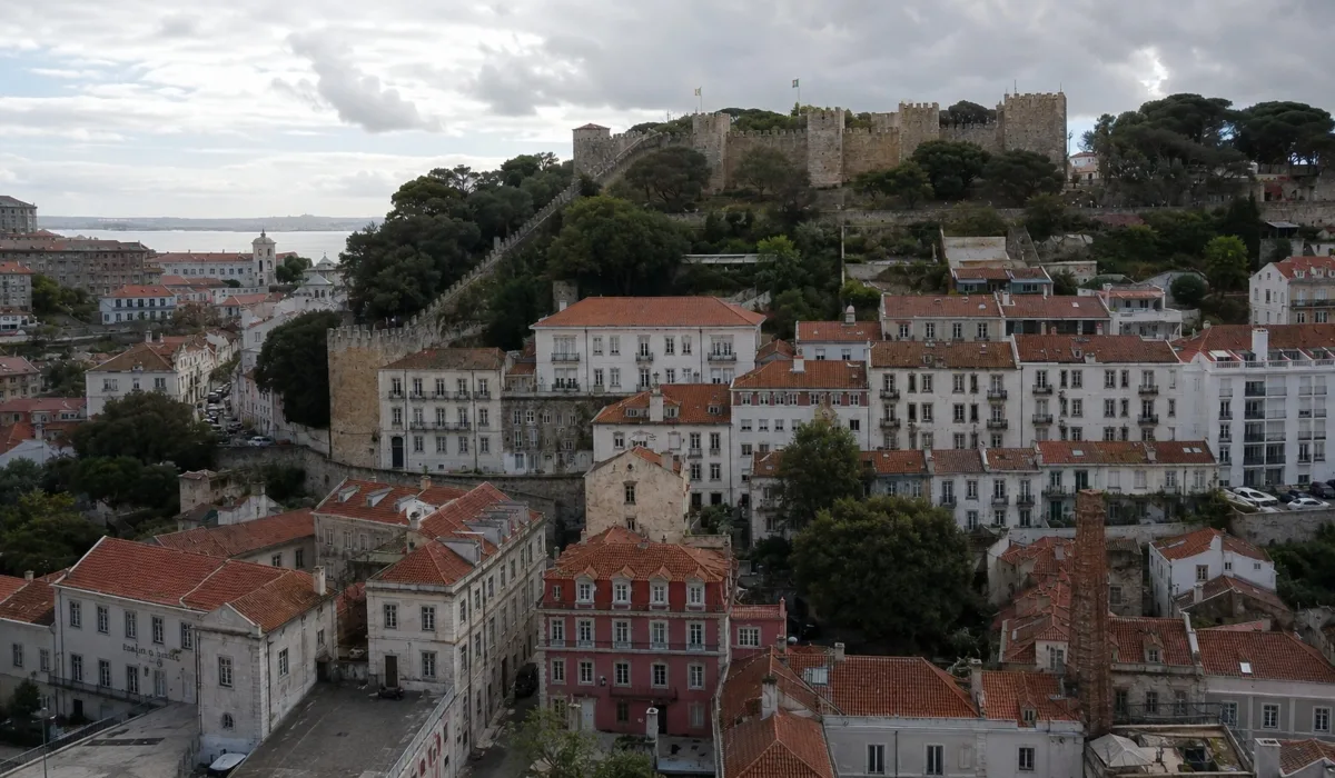 Vista panorámica del Castillo de San Jorge y el barrio de Alfama en Lisboa, con tejados tradicionales y ambiente histórico realista bajo un cielo nublado